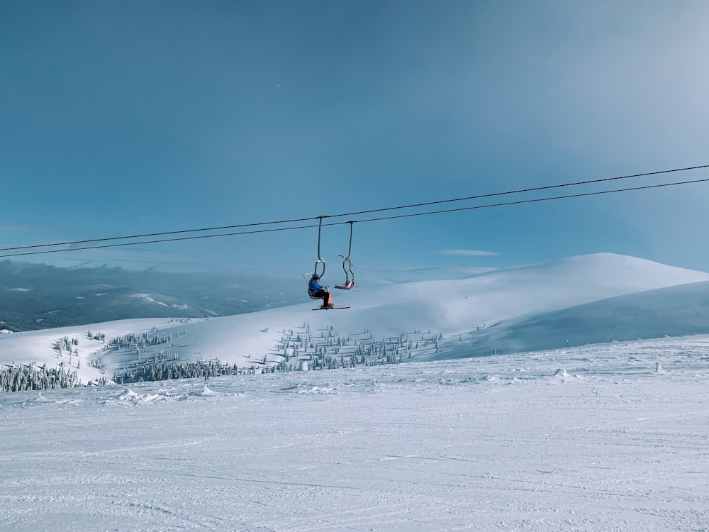 person in red jacket and blue pants riding on cable car over snow covered ground during