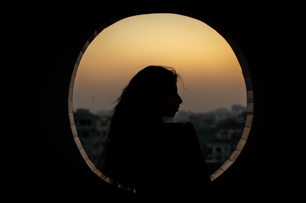 silhouette of woman standing near window during sunset