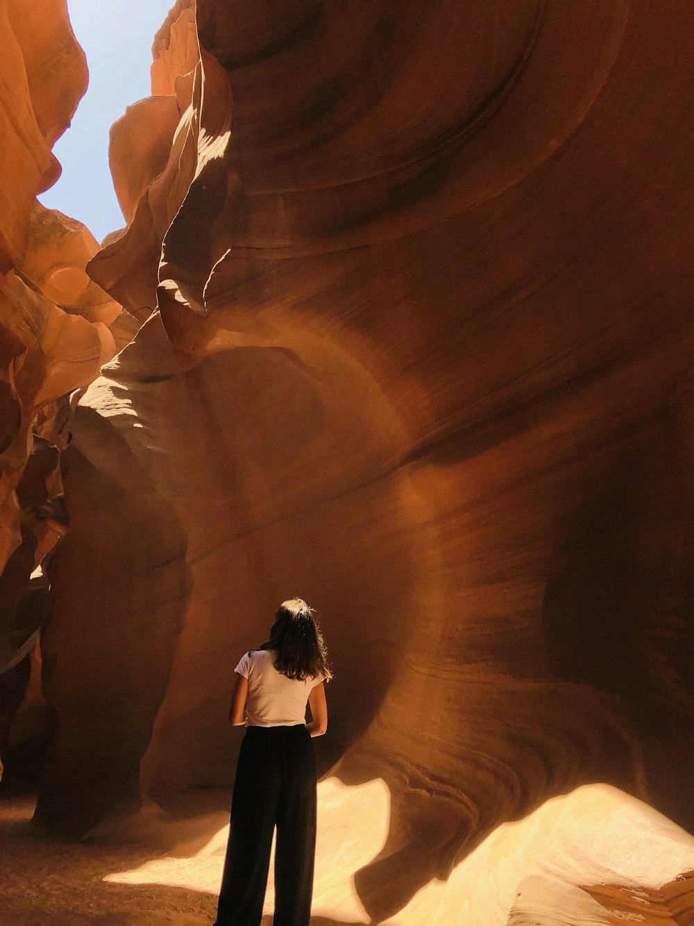 woman in white shirt and black pants standing in front of brown rock formation during daytime