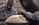 Two individuals, both wearing flannel shirts and hooded jackets, are engaged in playing a handpan. One of them is captured in motion, striking the instrument with their hands. The background is slightly blurred, giving the scene a sense of focus and intimacy on the musicians.