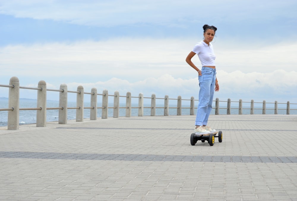 homem em regata branca e jeans azuis em pé no chão de concreto cinza durante o dia