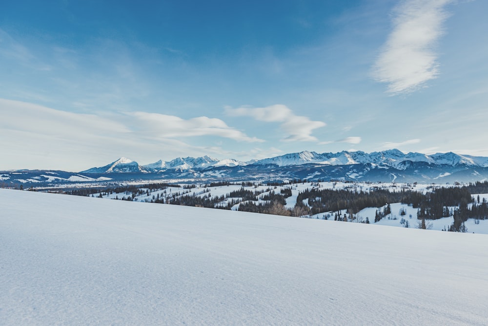 snow covered field and mountains under blue sky during daytime