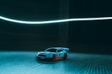 Close-up of a 1/28 scale RC car speeding on the banked straightaway under bright indoor lights.