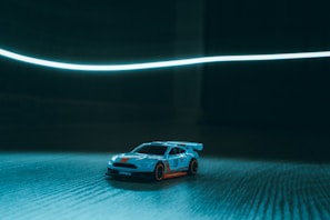 Close-up of a 1/28 scale RC car speeding on the banked straightaway under bright indoor lights