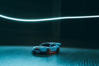 Close-up of a 1/28 scale RC car speeding on the banked straightaway under bright indoor lights