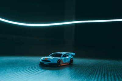 Close-up of a 1/28 scale RC car speeding on the banked straightaway under bright indoor lights.