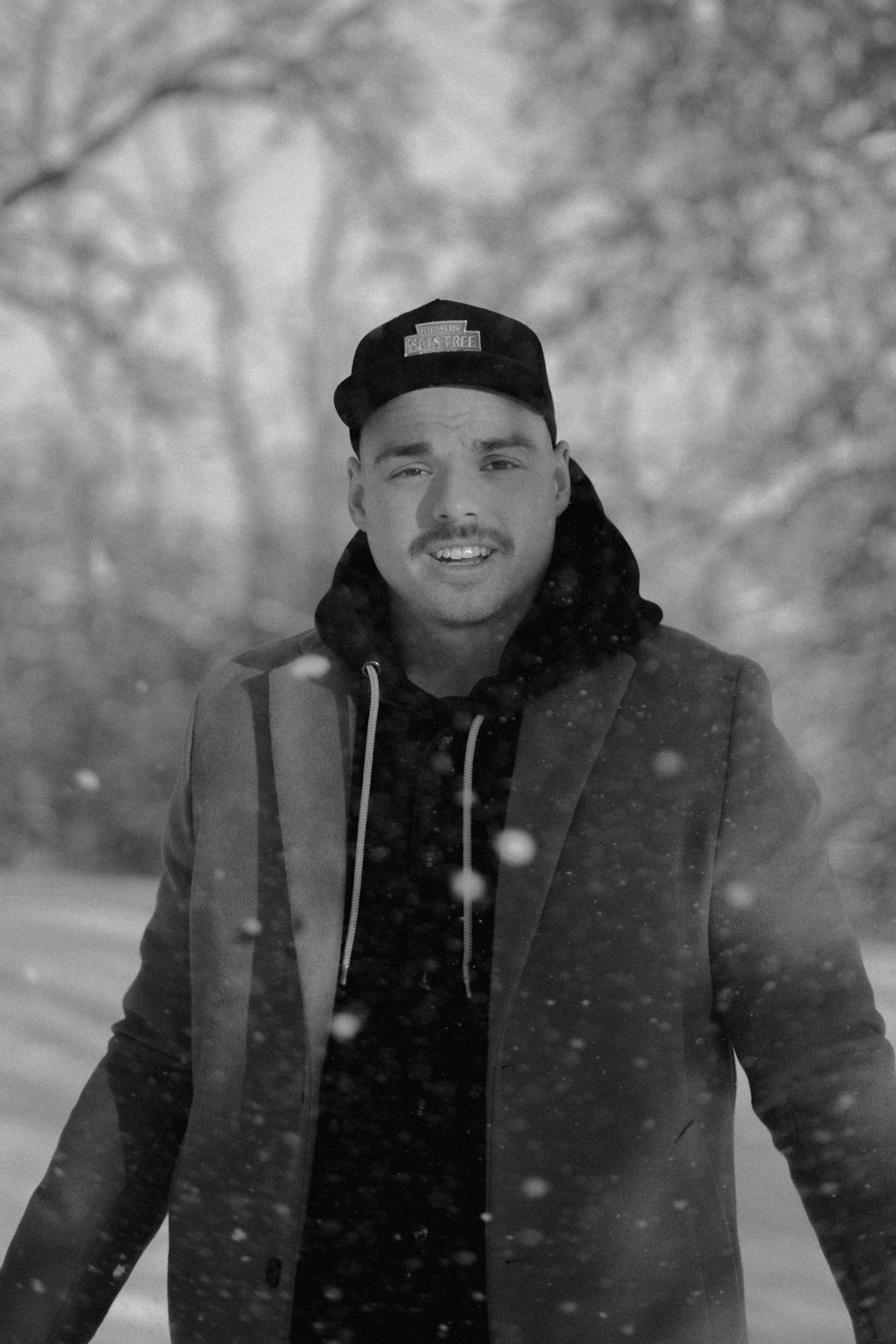 Foto in scala di grigi di uomo sorridente che indossa berretto e cappotto a maglia