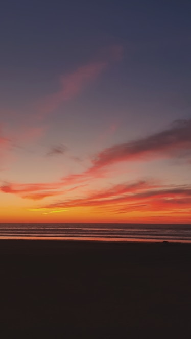 A breathtaking full-screen view of the sea at sunset with warm orange and pink hues blending into the horizon.