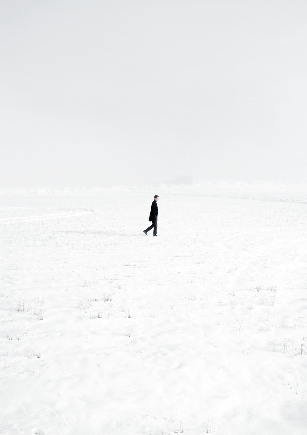 Person im schwarzen Kittel, die tagsüber auf einem schneebedeckten Feld spazieren geht