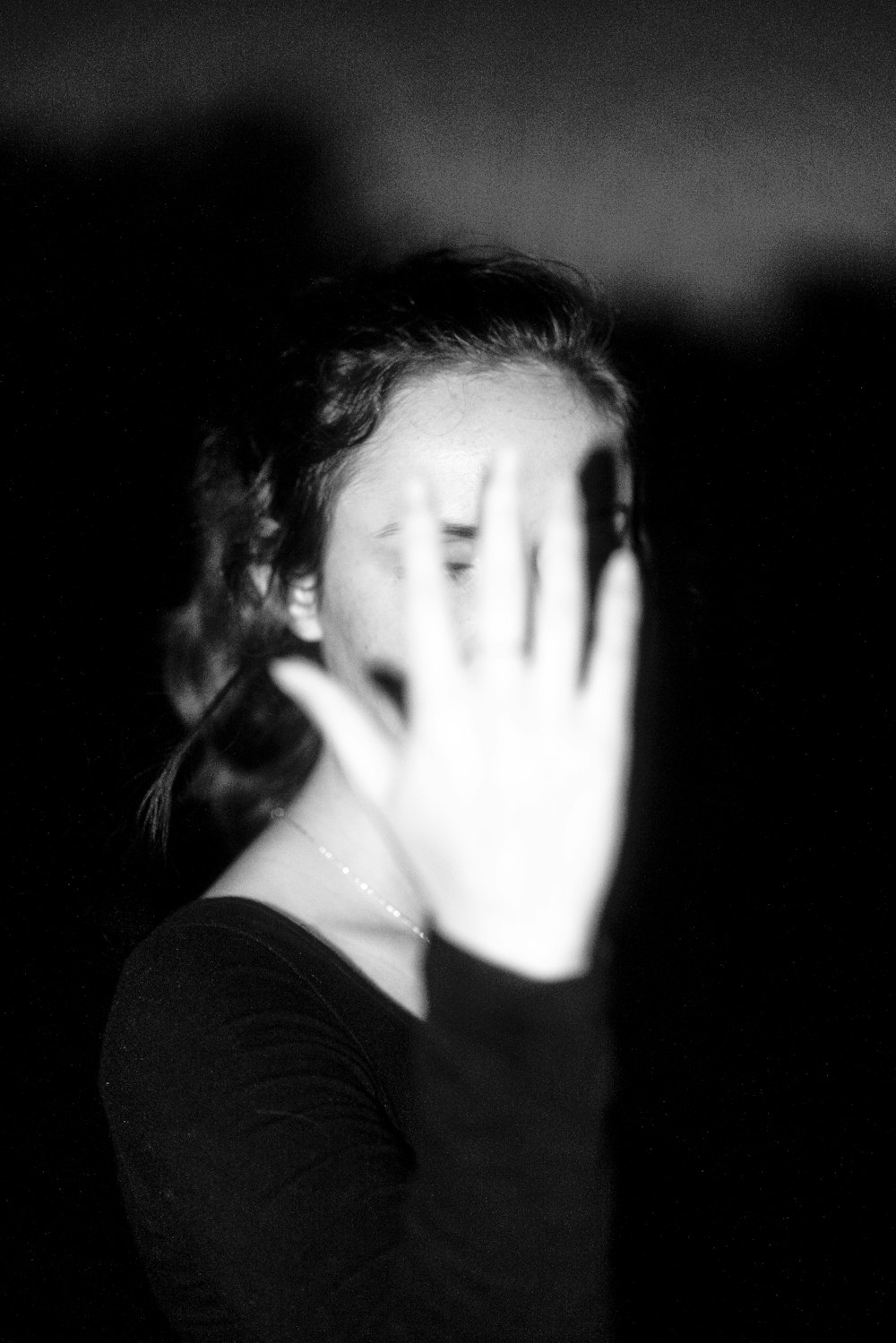 Frau in schwarzem Langarmhemd bedeckt ihr Gesicht mit den Händen