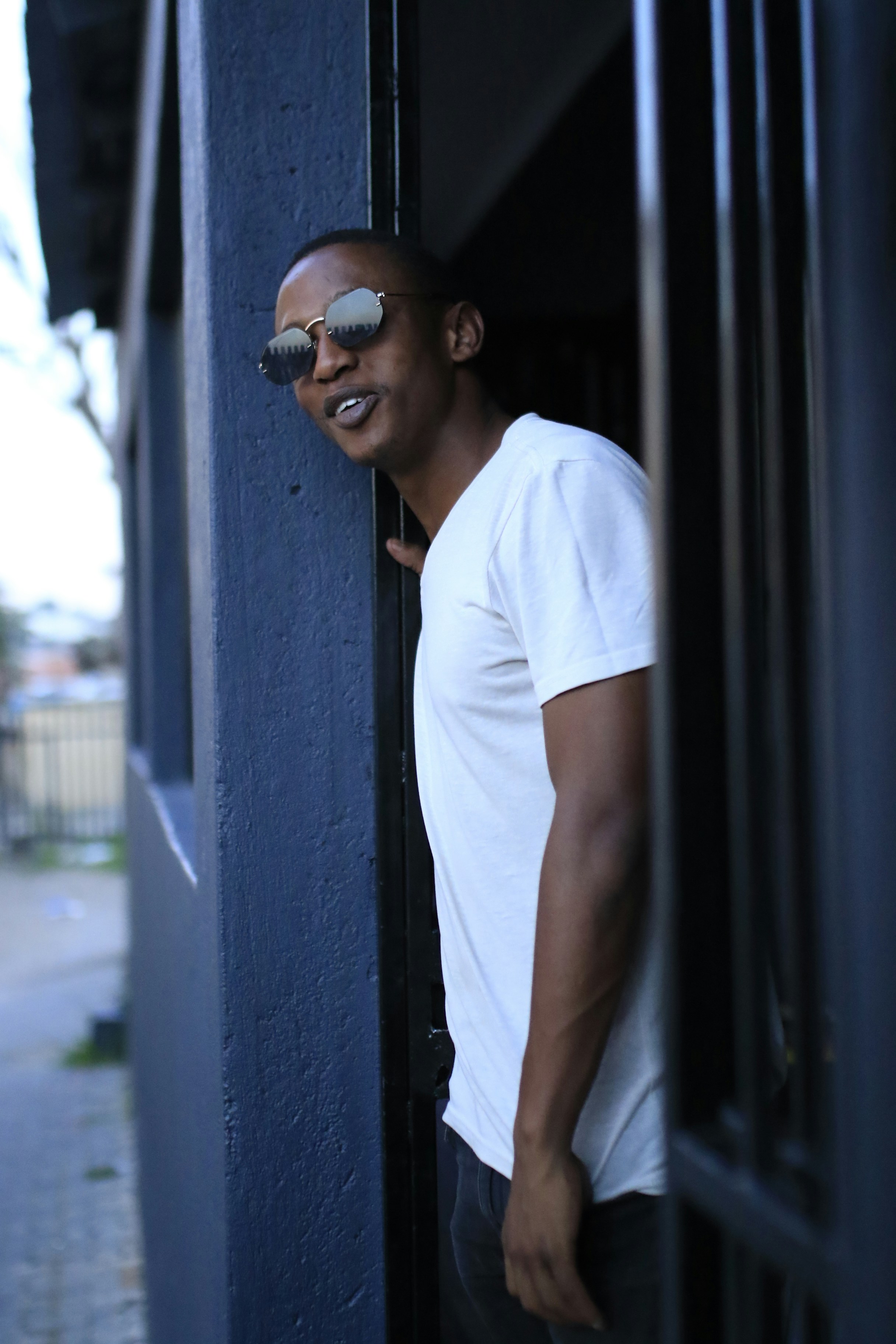 man in white crew neck t-shirt wearing black sunglasses standing beside gray wall during daytime