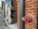 A brick wall with a red and metallic fire department connection labeled 'AUTO. SPKR. FIRE DEPT. CONNECTION' is prominently featured. The wall is adorned with colorful urban graffiti. Beside the brick wall, there is an alleyway with additional murals and street art.