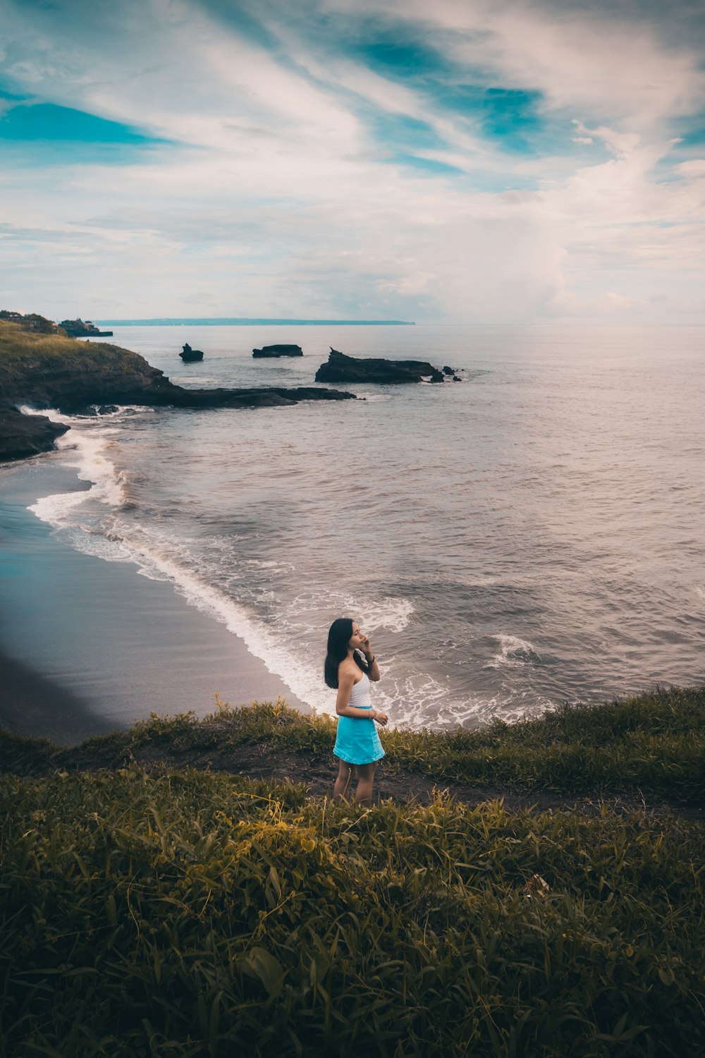 woman in blue denim shorts standing on green grass field near body of water during daytime