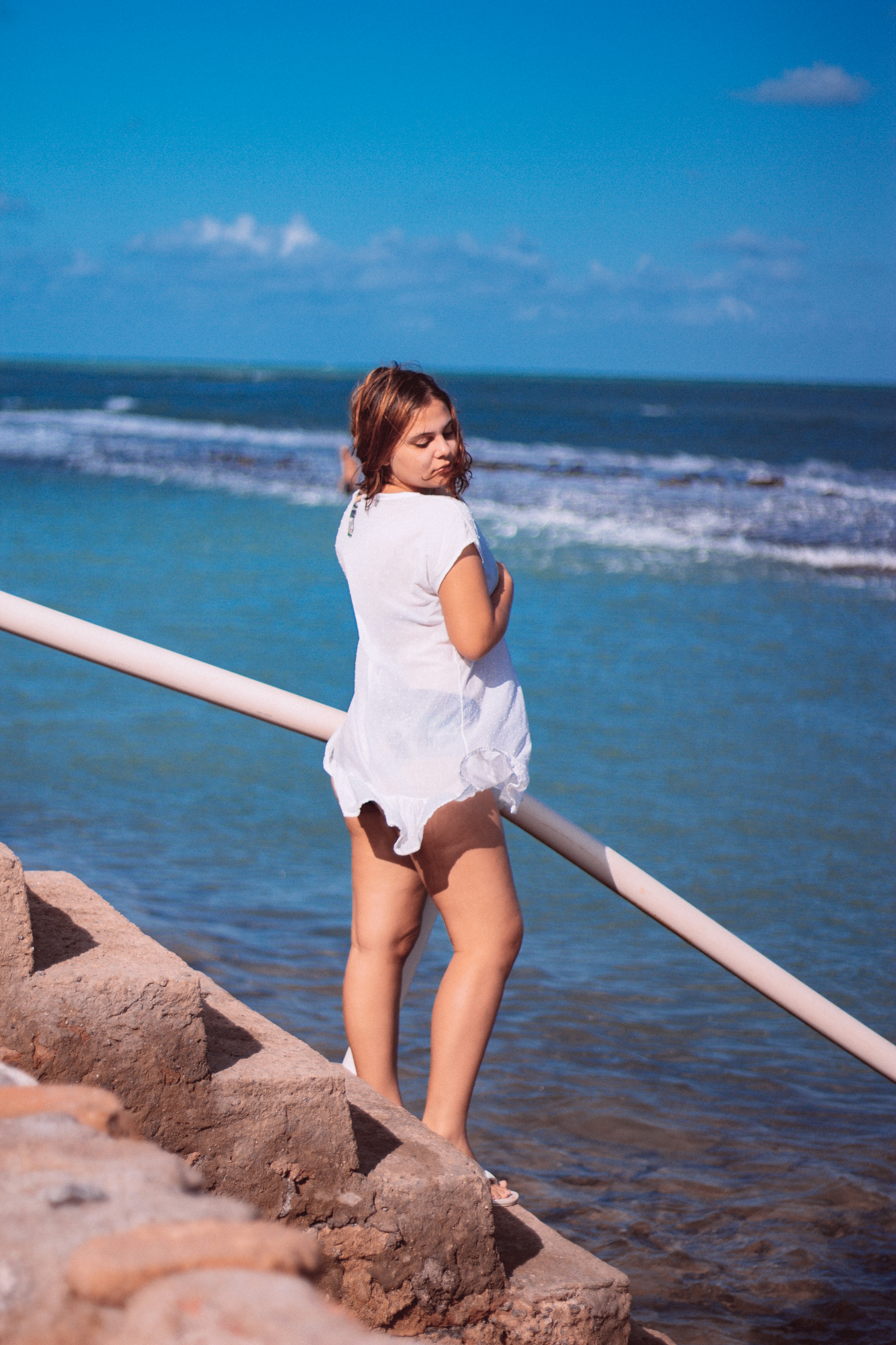 woman in white shirt and white shorts standing on brown rock near body of water during