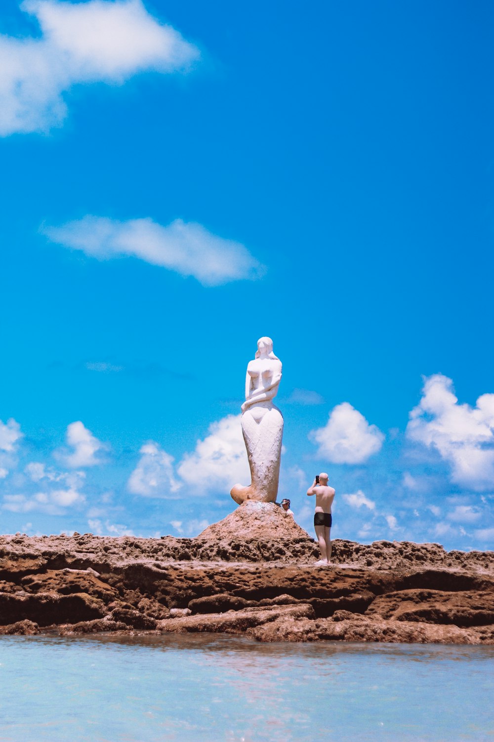 person in white long sleeve shirt and gray pants standing on brown rock under blue sky