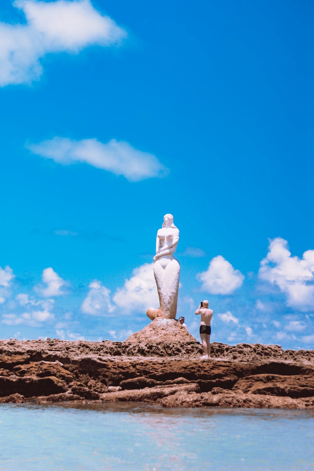 Person in weißem Langarmhemd und grauer Hose auf braunem Felsen unter blauem Himmel