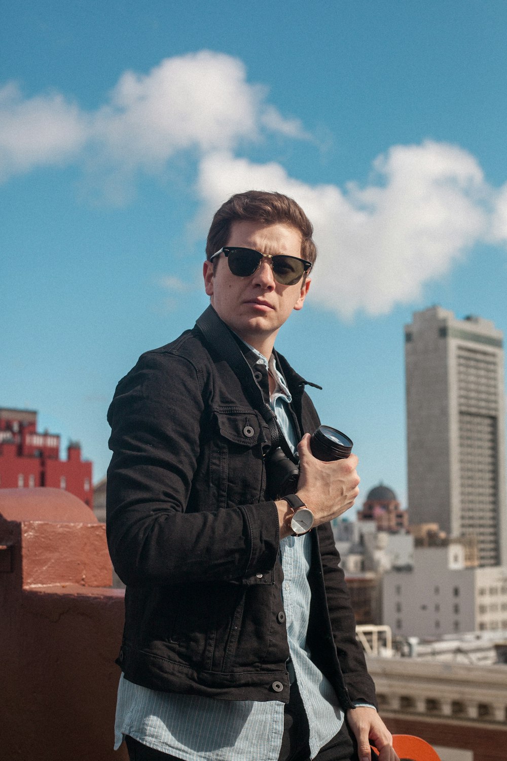 man in black coat wearing black sunglasses standing on top of building during daytime