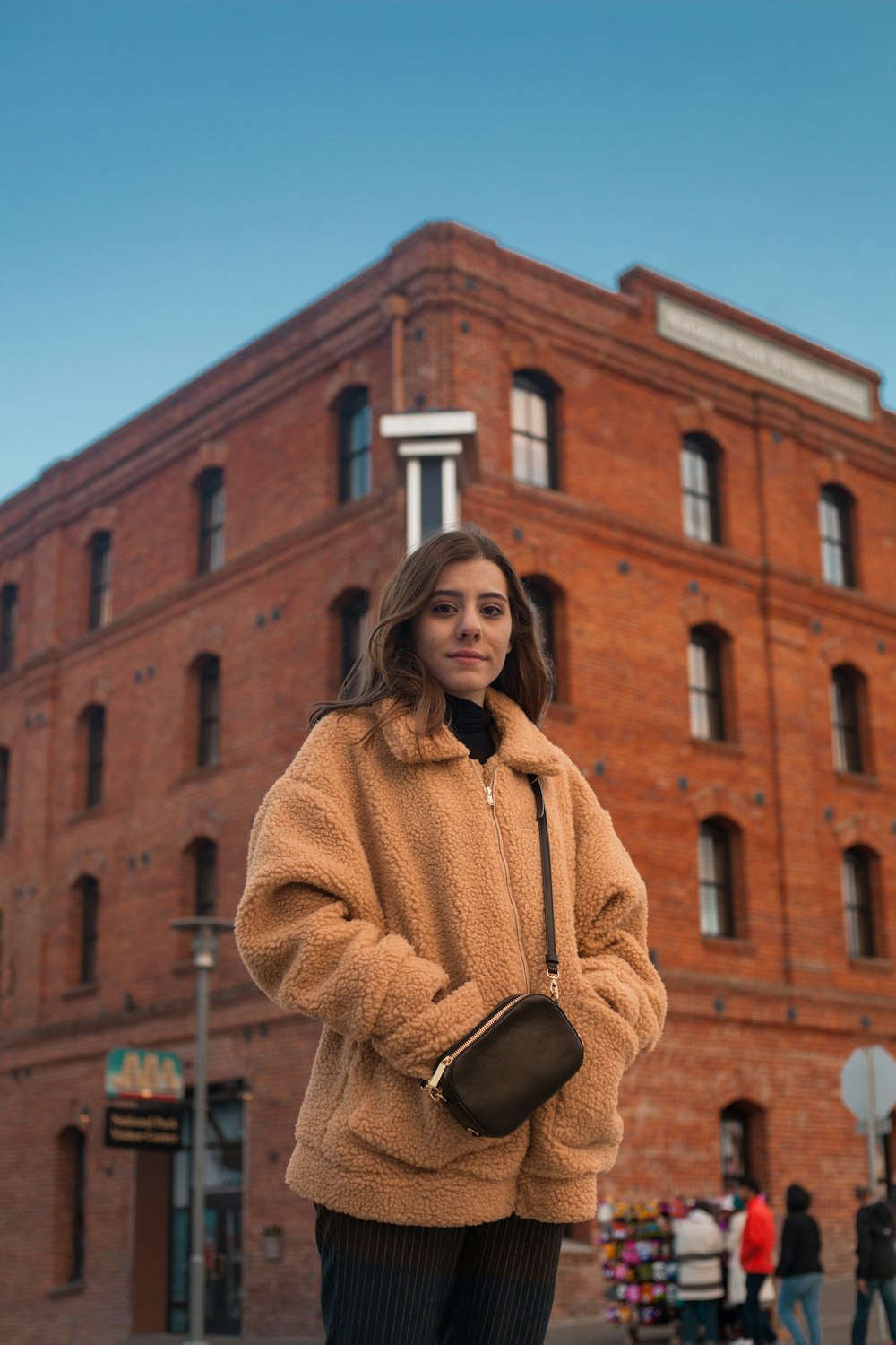 woman in yellow sweater standing near brown concrete building during daytime