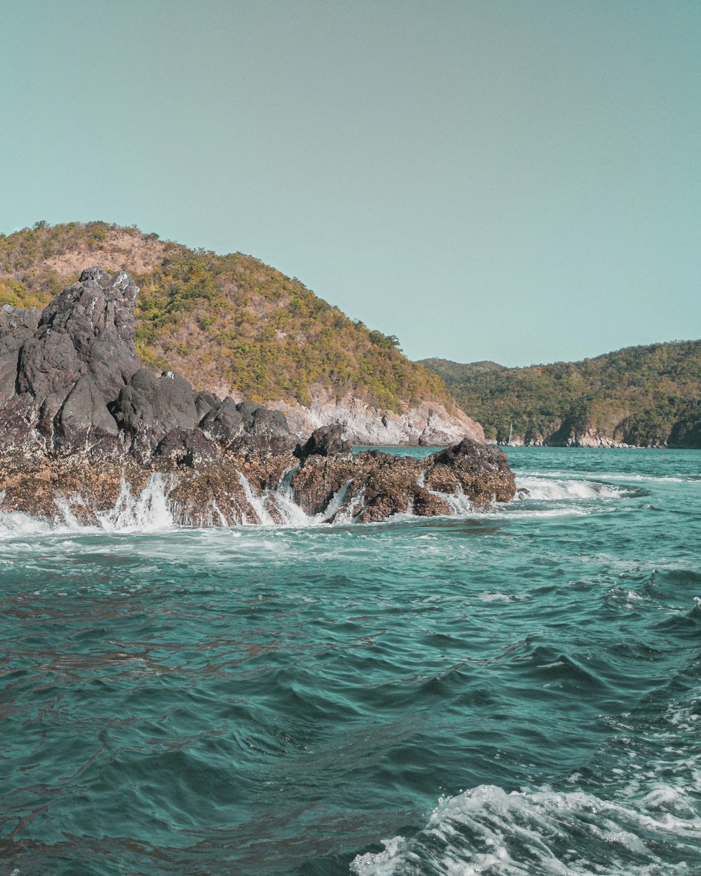 brown and green rock formation on body of water during daytime