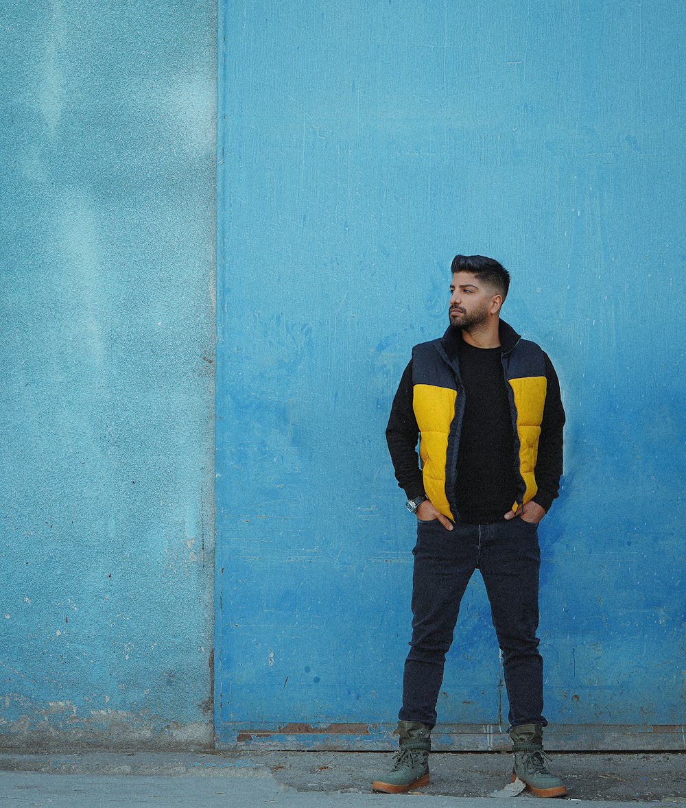 man in black and yellow long sleeve shirt and blue denim jeans standing beside blue painted