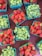 Brightly colored cartons filled with fresh strawberries and green grapes are arranged on a dark surface, creating a vibrant display. Each green carton is neatly packed with ripe, juicy strawberries or bunches of green grapes, showcasing a bountiful collection of fruit.