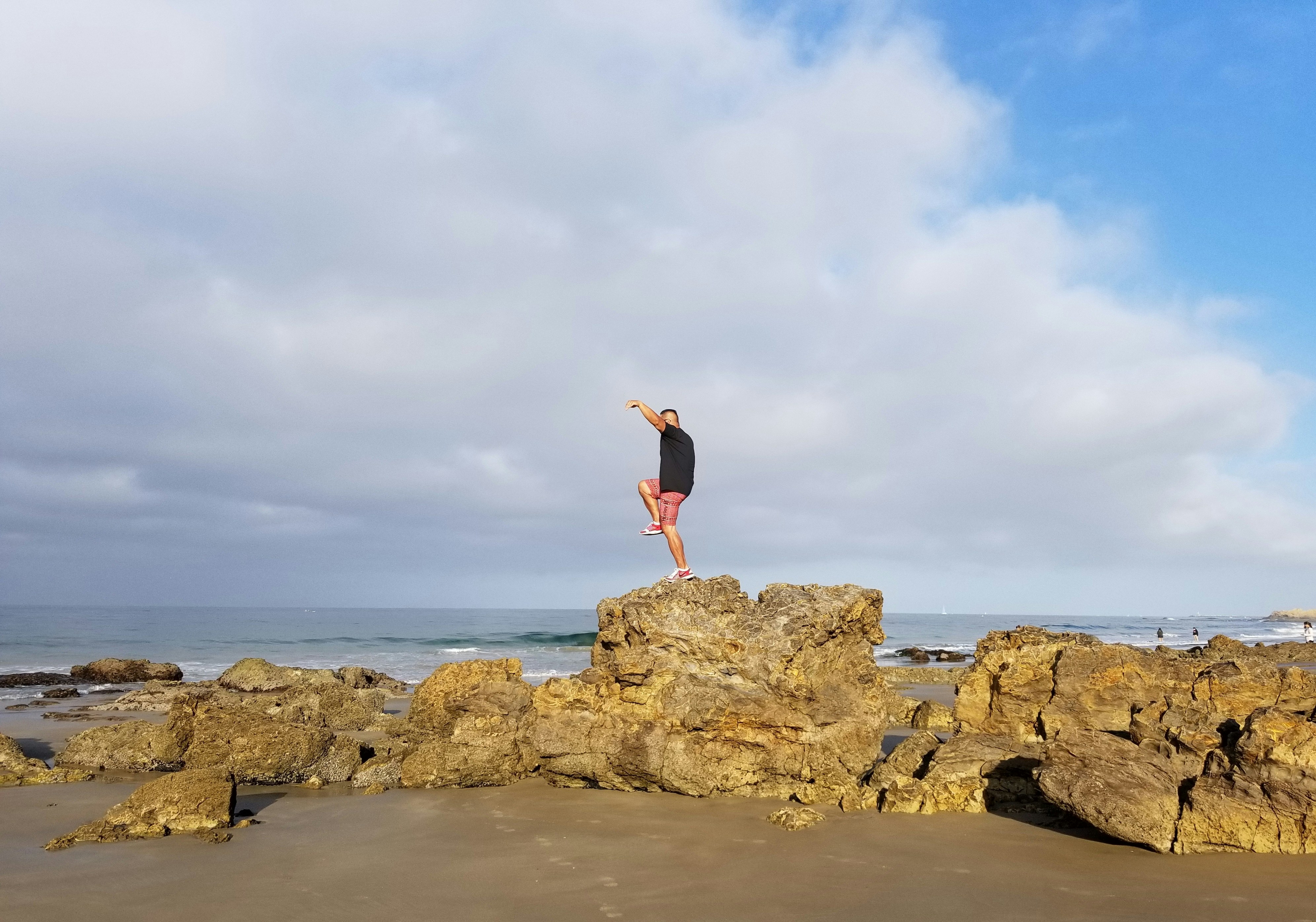 woman in red tank top and black shorts standing on brown rock formation during daytime