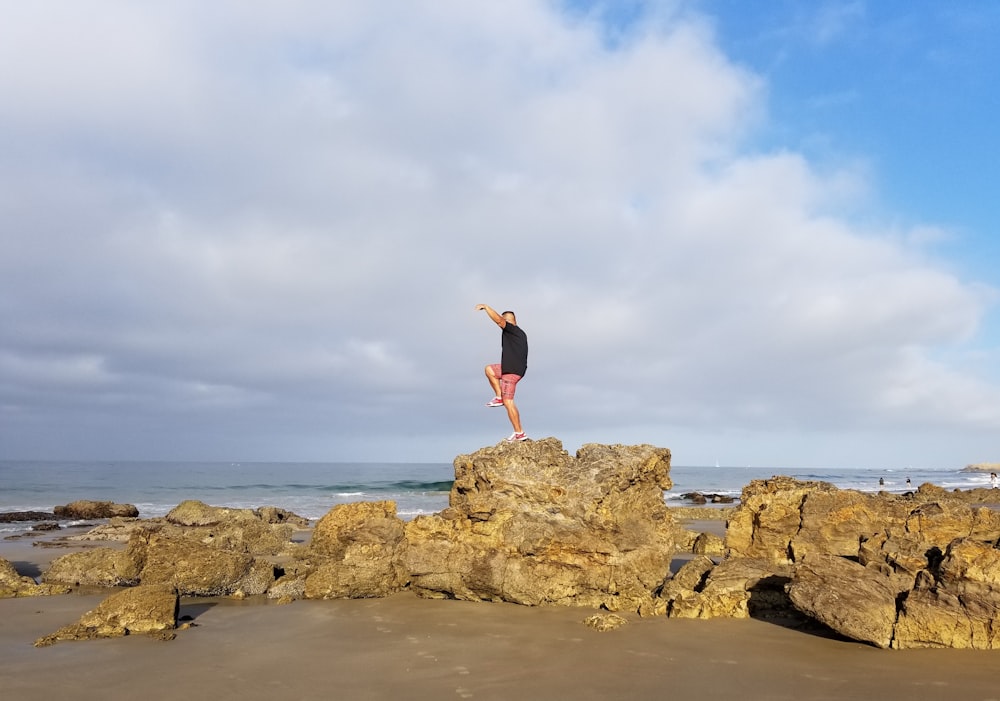 woman in red tank top and black shorts standing on brown rock formation during daytime