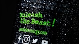 There is text written in a bold, green font that reads 'Unleash the Beast!' along with the website 'monsterenergy.com'. The background is dark with water droplets scattered across the surface. Several social media icons are visible at the bottom.