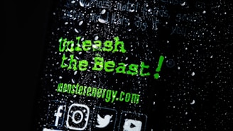 There is text written in a bold, green font that reads 'Unleash the Beast!' along with the website 'monsterenergy.com'. The background is dark with water droplets scattered across the surface. Several social media icons are visible at the bottom.