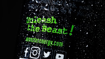 There is text written in a bold, green font that reads 'Unleash the Beast!' along with the website 'monsterenergy.com'. The background is dark with water droplets scattered across the surface. Several social media icons are visible at the bottom.