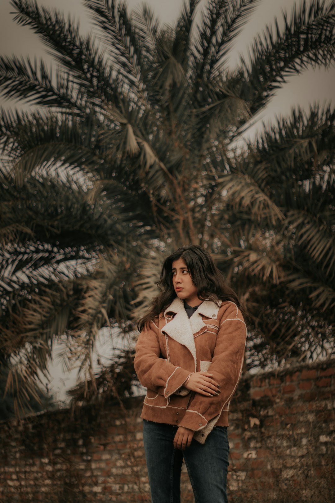 woman in brown coat standing near green pine tree during daytime