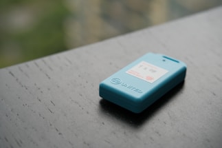 A small blue electronic device rests on a dark wooden surface. It features a display with text and a logo, and the word 'UNITED' is engraved on its side.