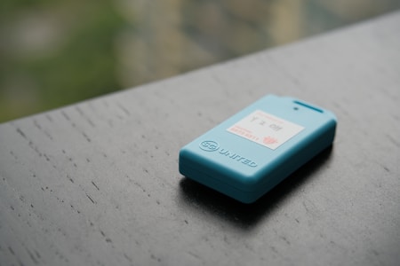 A small blue electronic device rests on a dark wooden surface. It features a display with text and a logo, and the word 'UNITED' is engraved on its side.