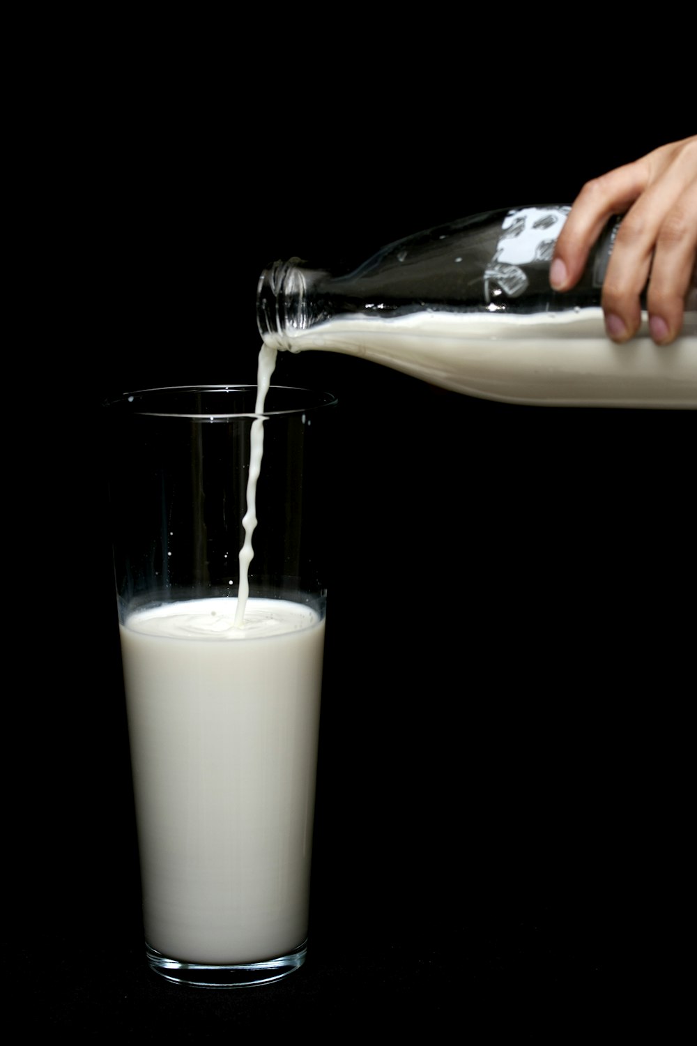 person pouring milk on clear drinking glass