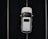 Aerial view of a white car parked in a space outlined by parallel white lines on a dark asphalt surface.