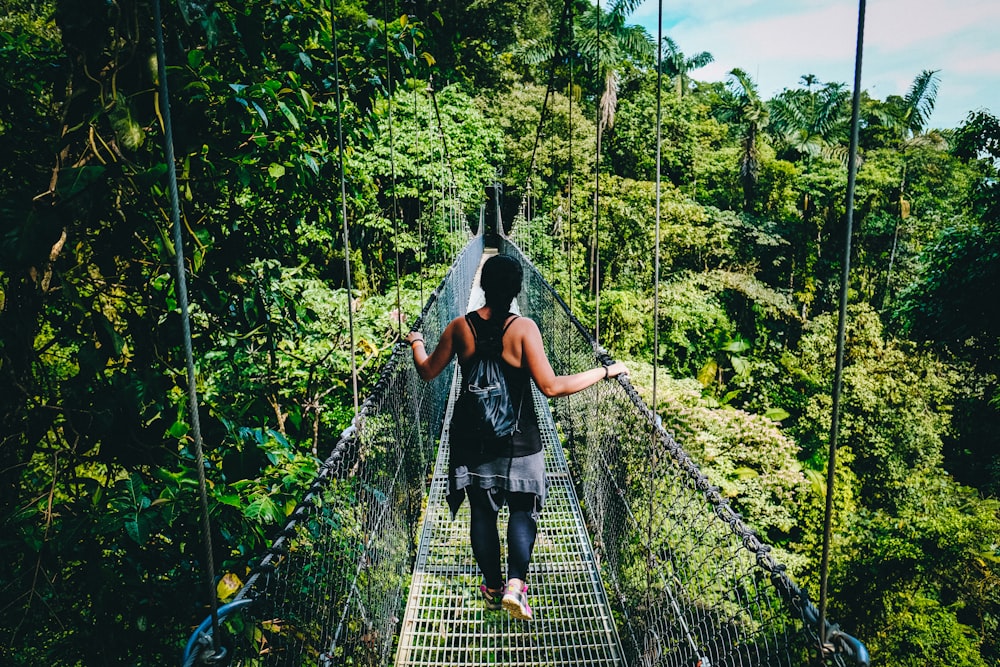 Mujer con camisa negra y pantalones negros de pie en un puente colgante