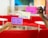 Three hands hold up colorful sticky notes labeled 'To Do', 'Doing', and 'Done' against a blurred background of red seating and a modern office environment.