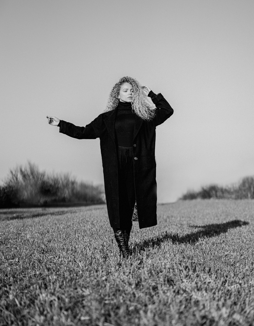 grayscale photo of woman in black coat standing on grass field