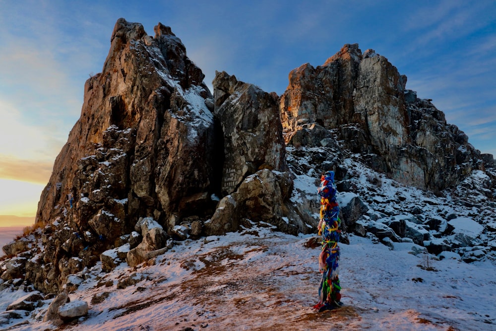 Persona in giacca blu e rossa in piedi sulla collina rocciosa durante il giorno