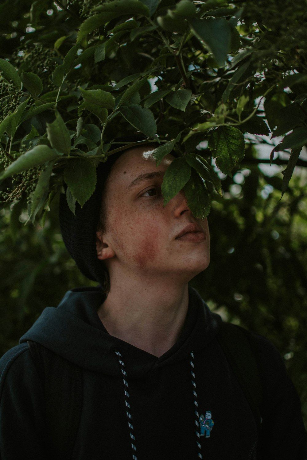 man in black jacket and black hat standing under green tree during daytime