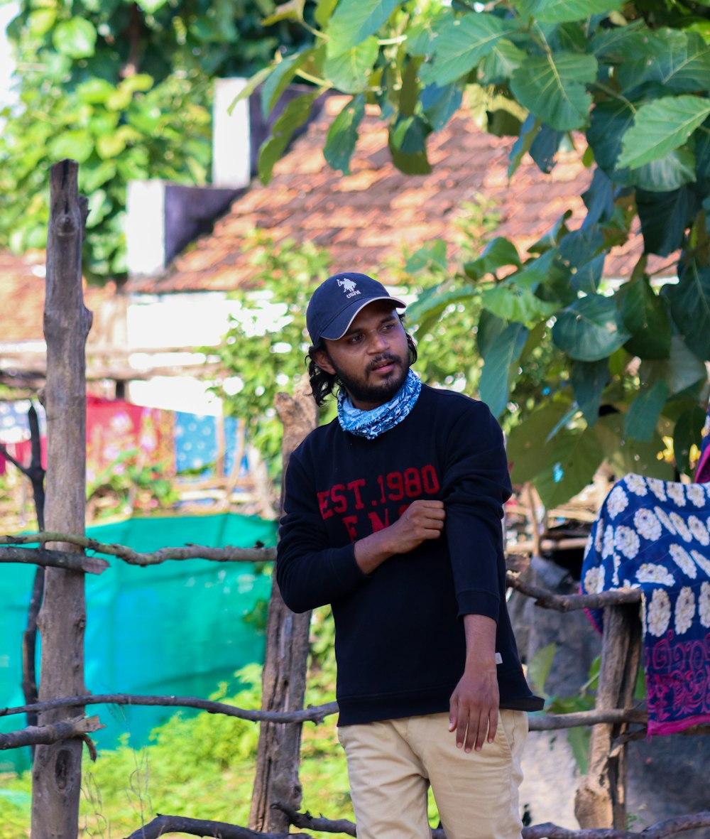 man in black and red crew neck t-shirt and brown pants standing beside green wooden