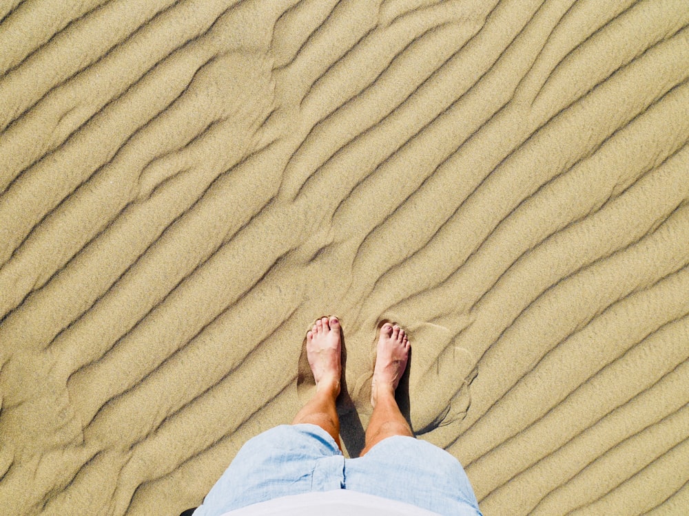 pessoa em calças brancas em pé na areia marrom