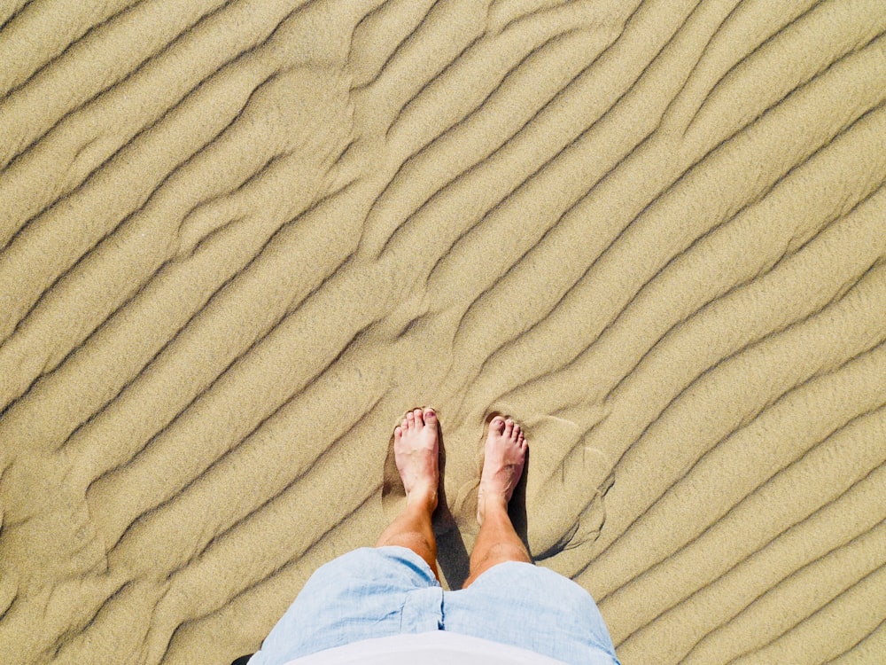 person in white pants standing on brown sand