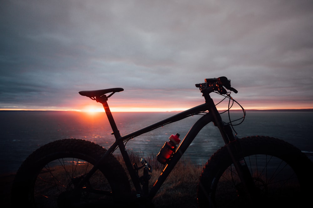 日没時の水域近くの黒と赤のハードテイルマウンテンバイク