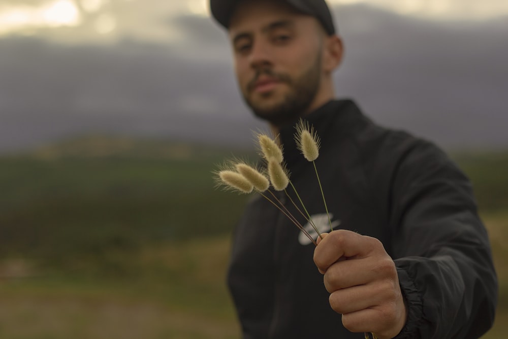 man in black jacket holding white dandelion during daytime