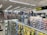 A well-lit store interior filled with fishing and outdoor equipment. The shelves are stocked with various lures, fishing lines, and other accessories. A range of colorful life vests is displayed on the back wall. A caution sign and a digital temperature display are mounted near the ceiling.