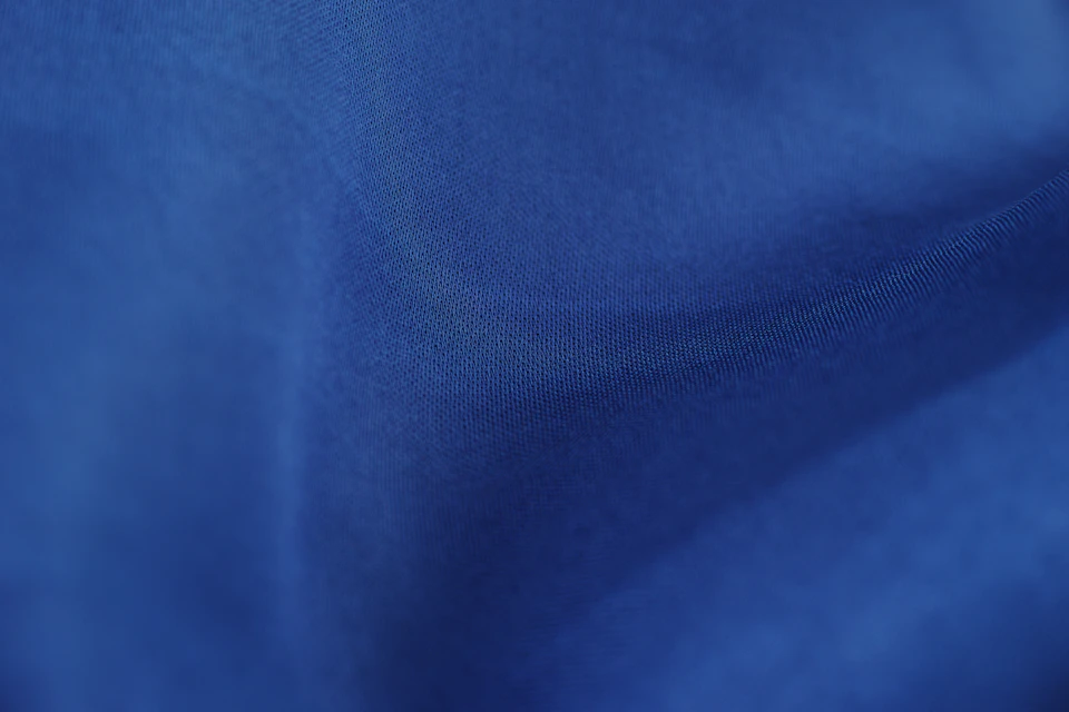 Close-up view of blue, wrinkled fabric folded over itself on a light brown background