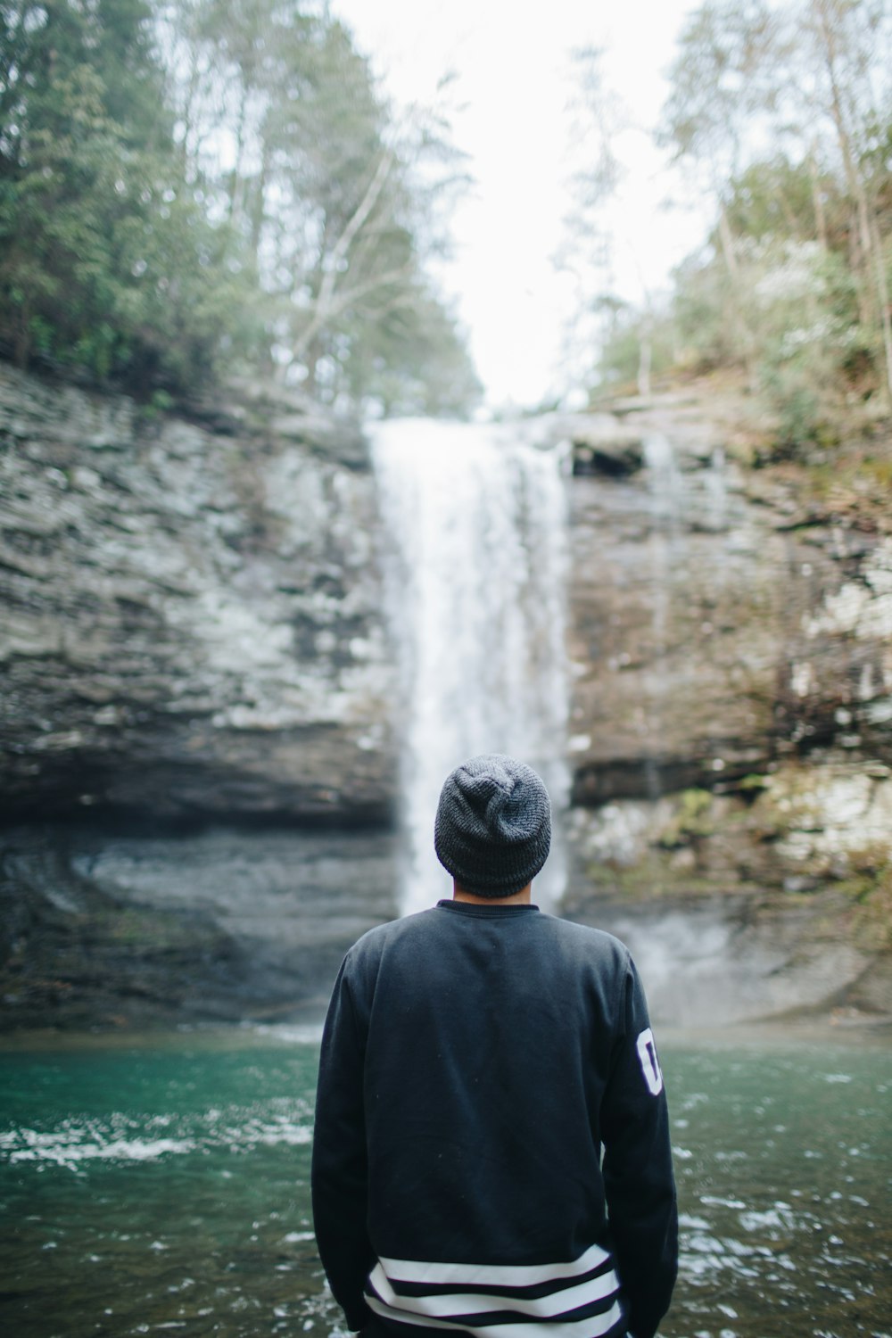 homem na jaqueta preta em pé perto de cachoeiras durante o dia