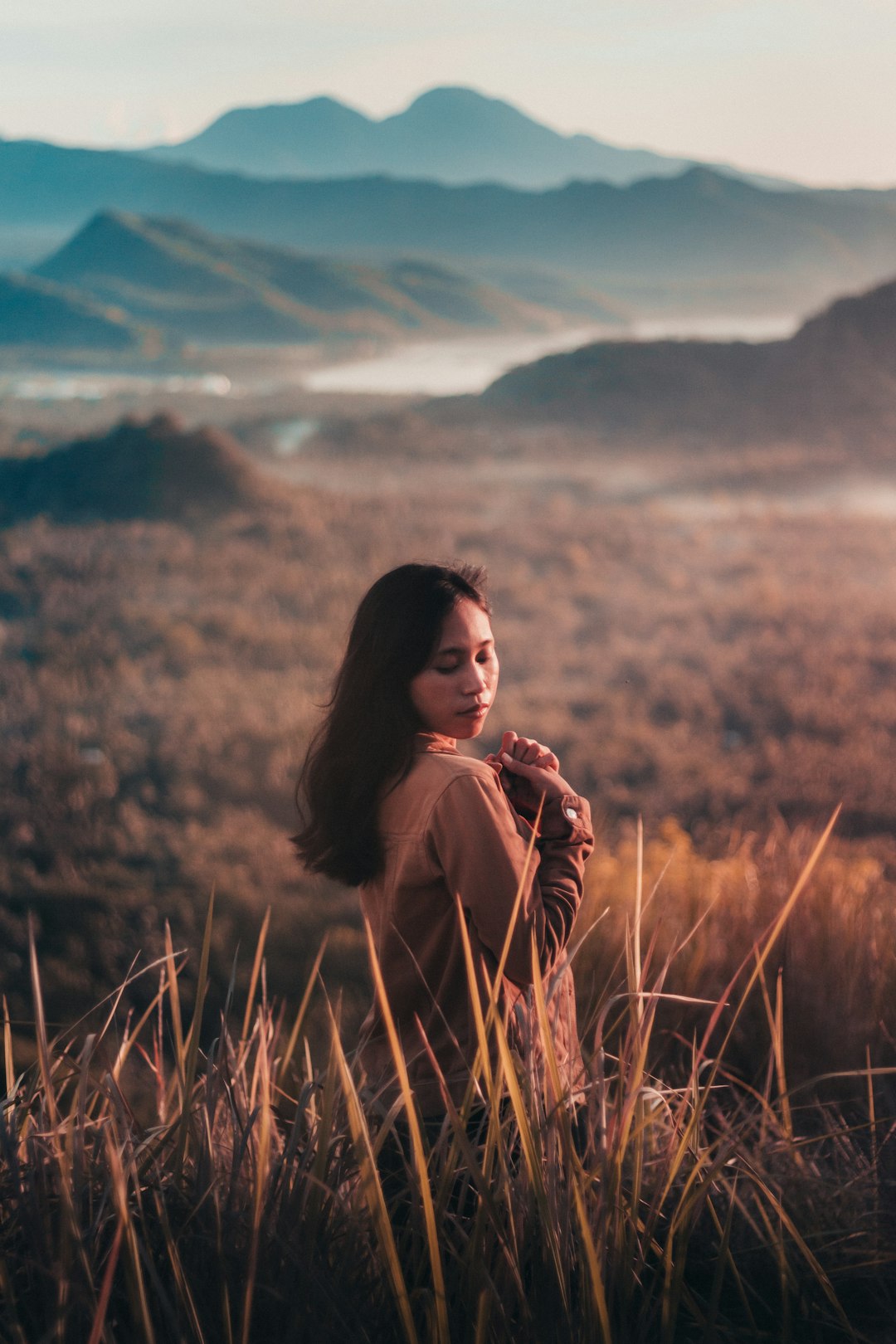 woman in brown jacket standing on brown grass field during daytime