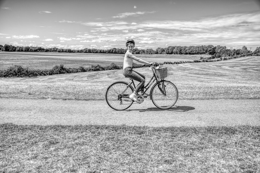 grayscale photo of man riding on bicycle on road